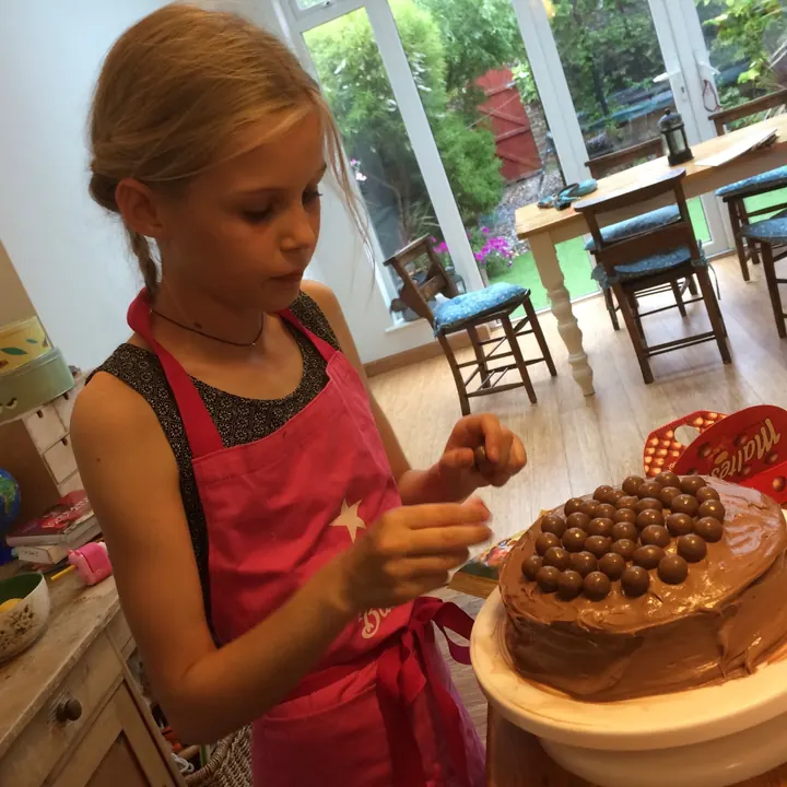 Young Martha in a pink apron decorating a Malteser birthday cake