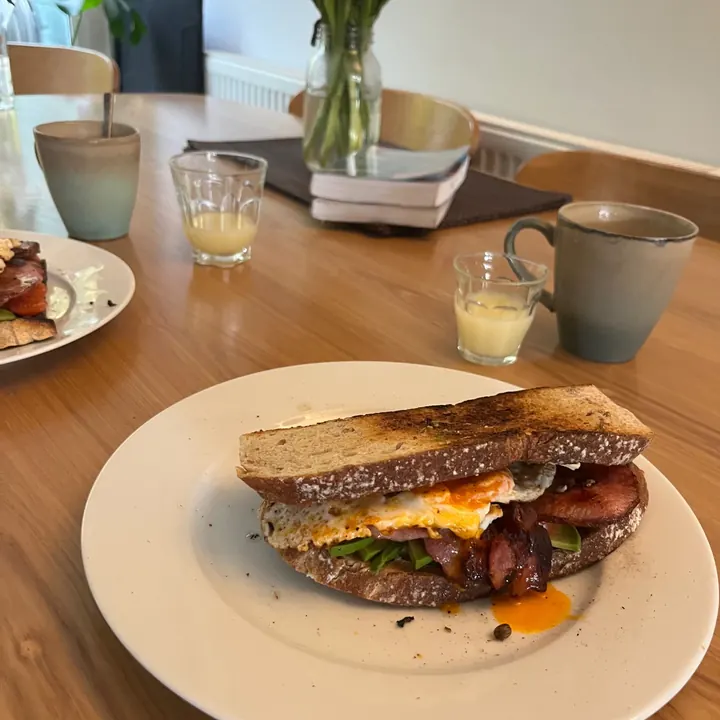 A breakfast sandwich with ginger shots, mugs of tea and flowers