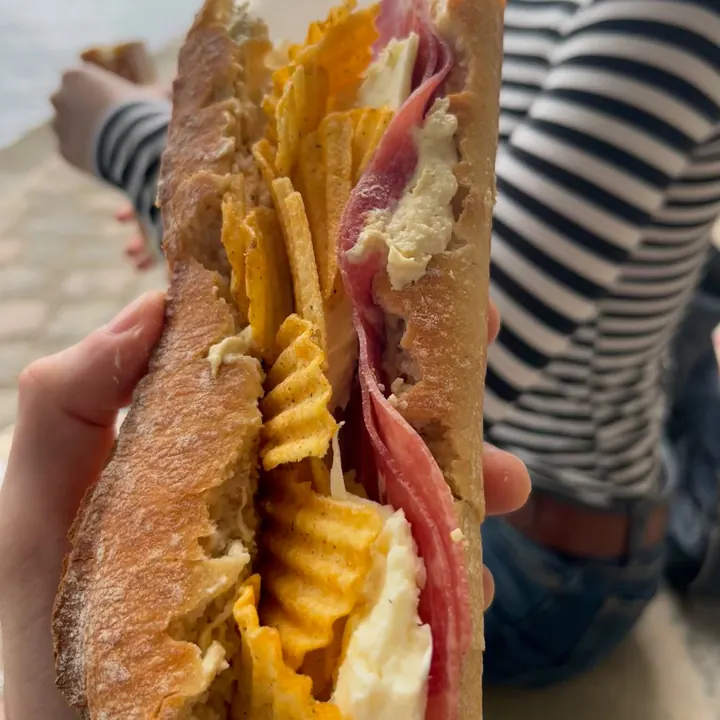 A crisp-filled baguette sandwich held up by the Seine